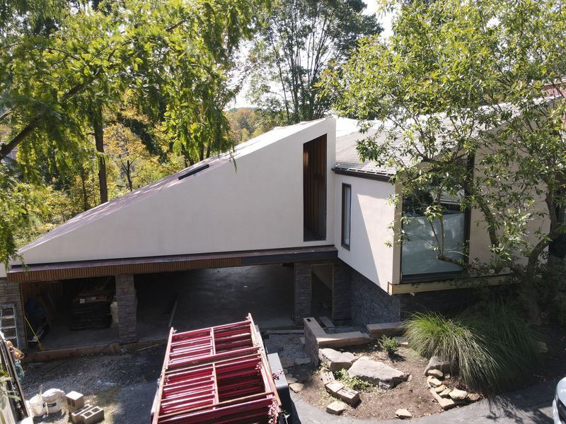 Modern house with angled roof, off-white walls, built into trees. Open car port below.