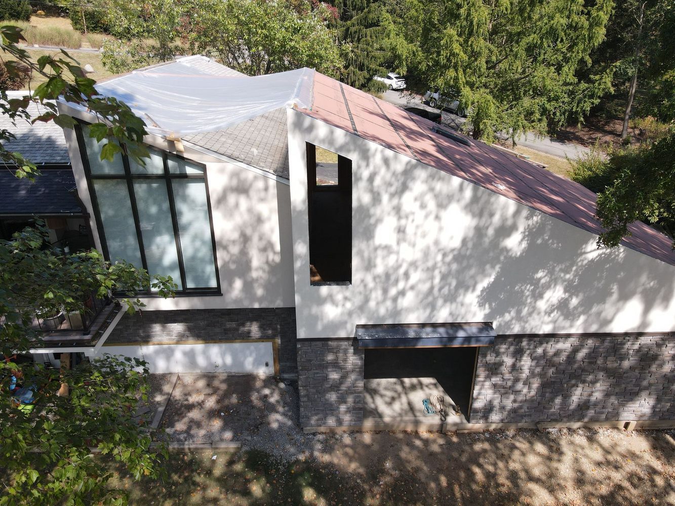 Modern white and grey house with angled roof and large windows surrounded by trees.