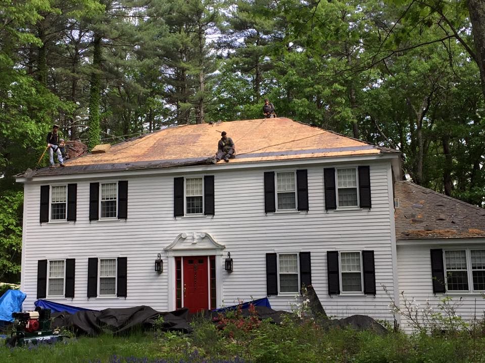 Two men are working on the roof of a white house.