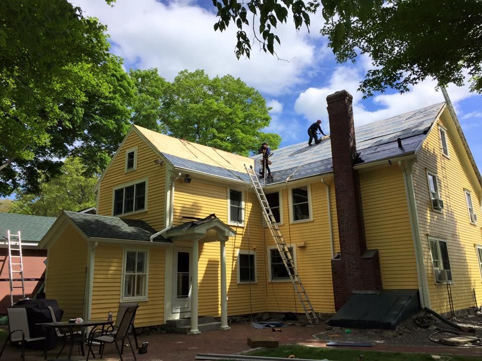 Two men are working on the roof of a yellow house