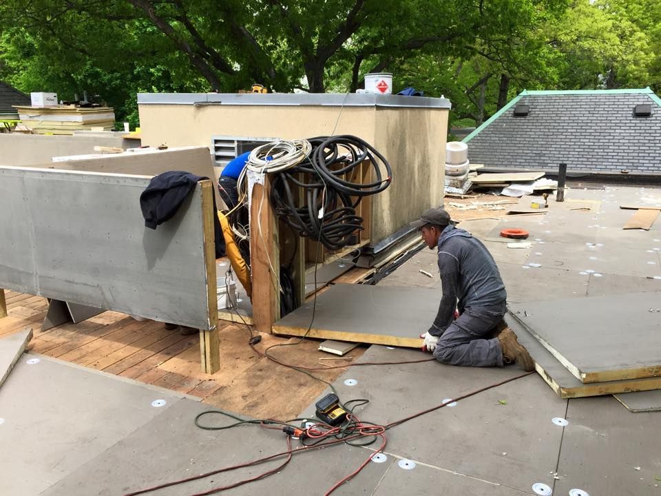 A man is kneeling on the ground working on a roof.