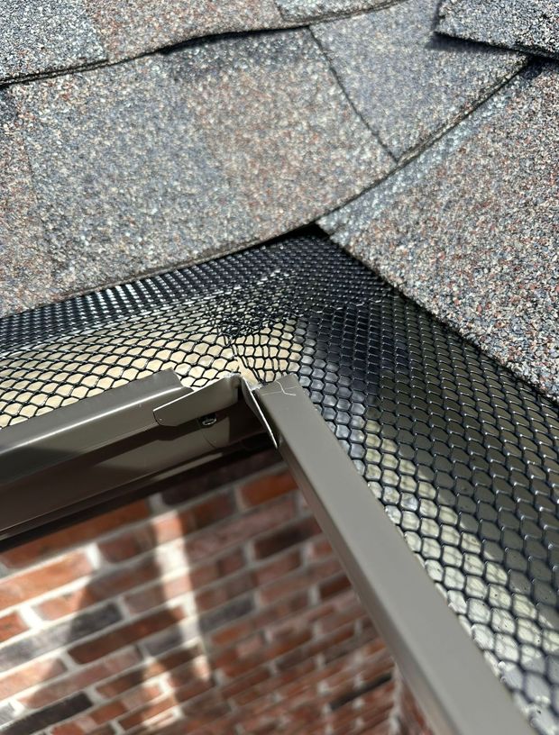 Close-up of a shingled roof edge with black metal flashing above a brick wall.