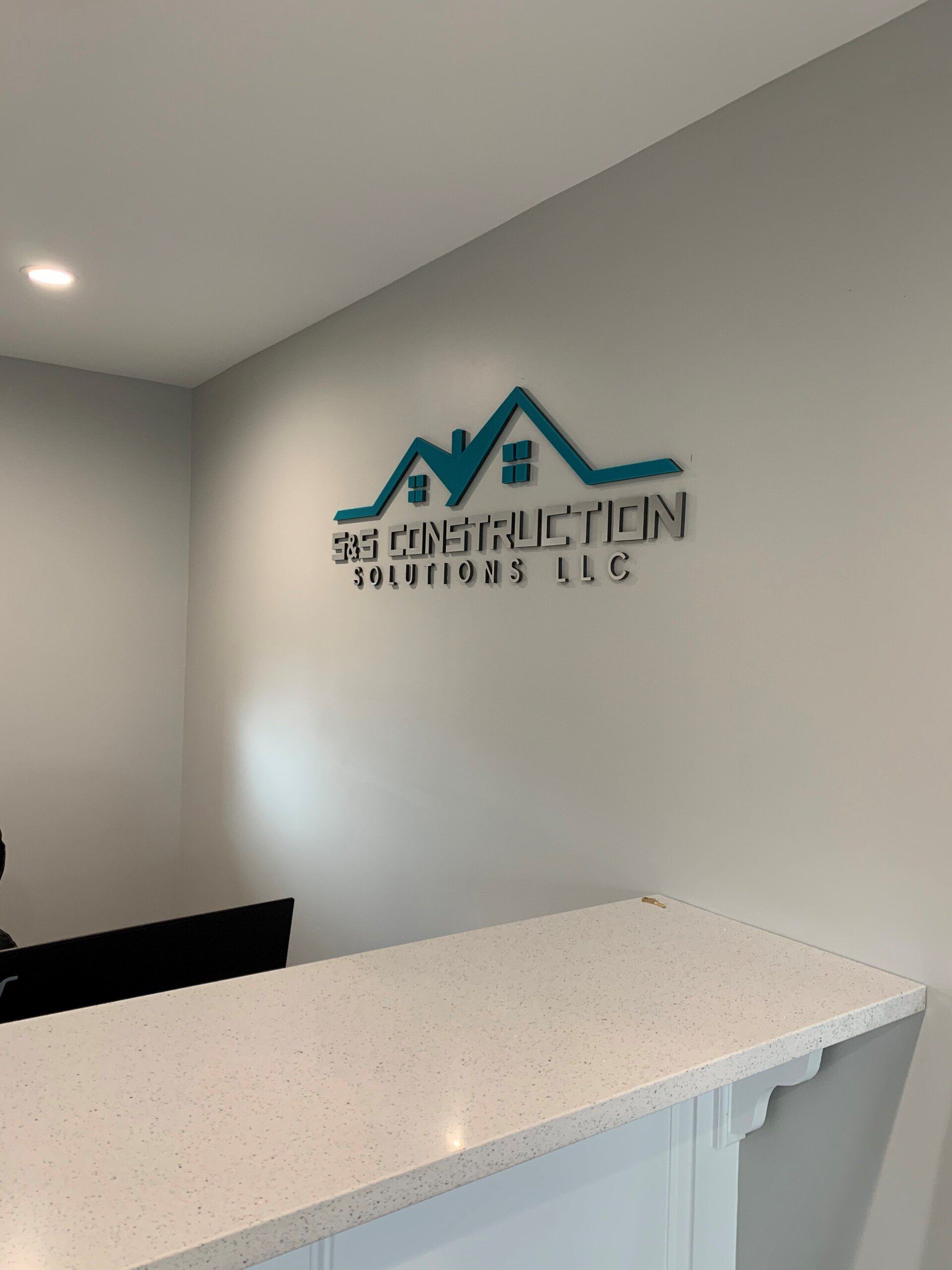 Reception area with a white countertop and a company logo on the wall: blue house outline above the text 