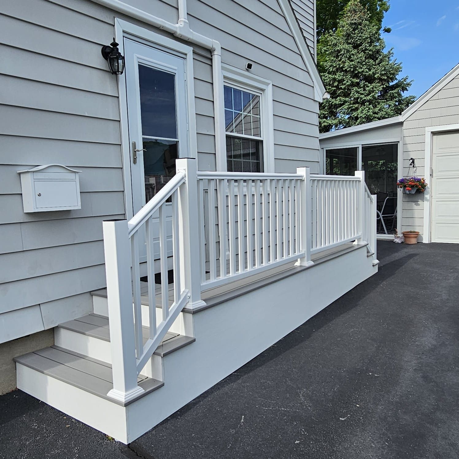 A white, slatted railing surrounds a small porch with steps leading to a gray house's front door. The porch is painted light gray.