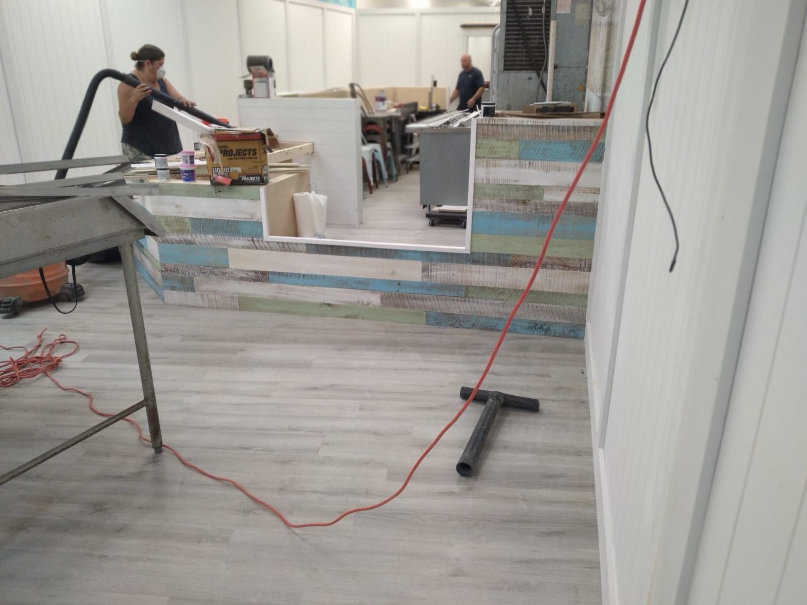 People cleaning a brightly lit interior space. One vacuums, while another works in the background near a countertop.