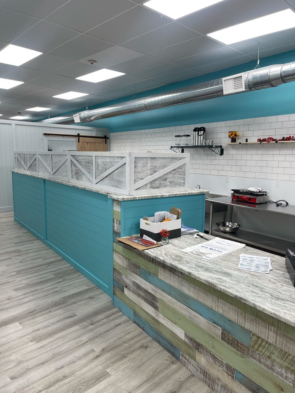 Interior view of a restaurant or shop with blue and white accents, rustic wood paneling, and a counter with a speckled countertop.