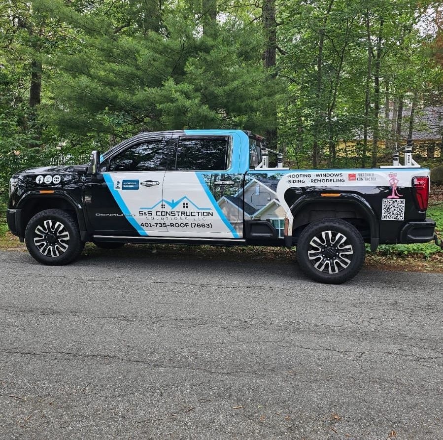 Black and blue pickup truck with company logo parked on gravel driveway, trees in the background.