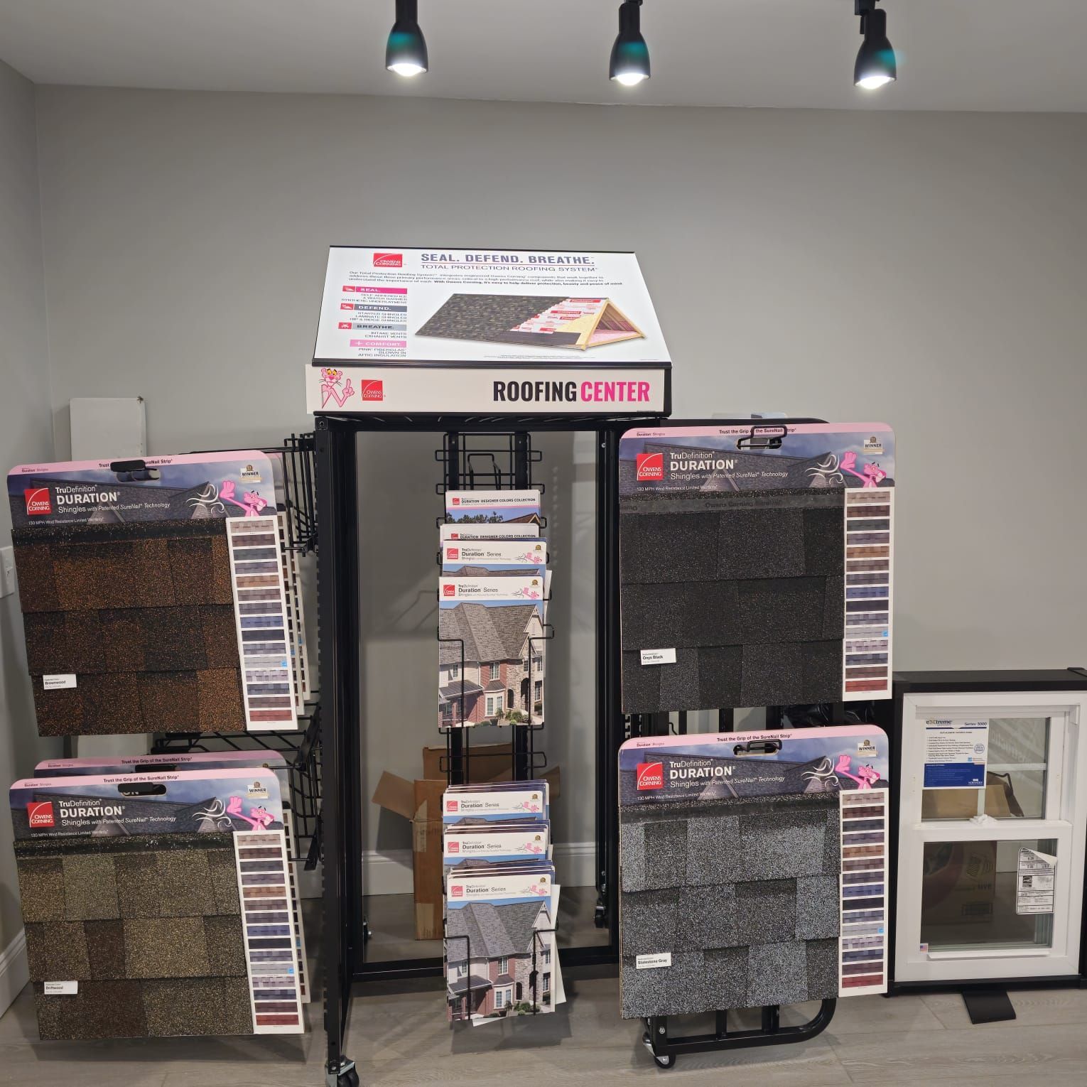 Display stand at a roofing center showcasing various shingle colors and a window frame.