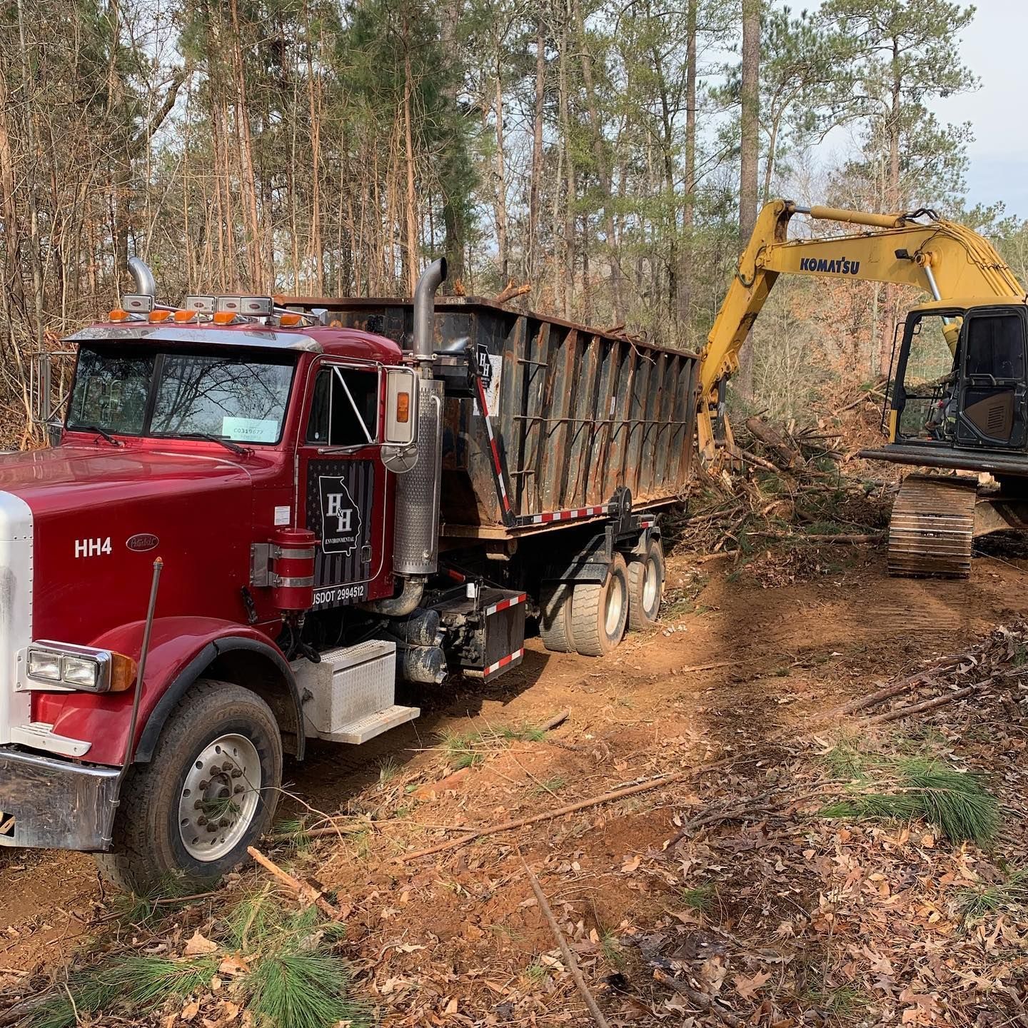 Red dump truck and yellow excavator working on a dirt road in a wooded area