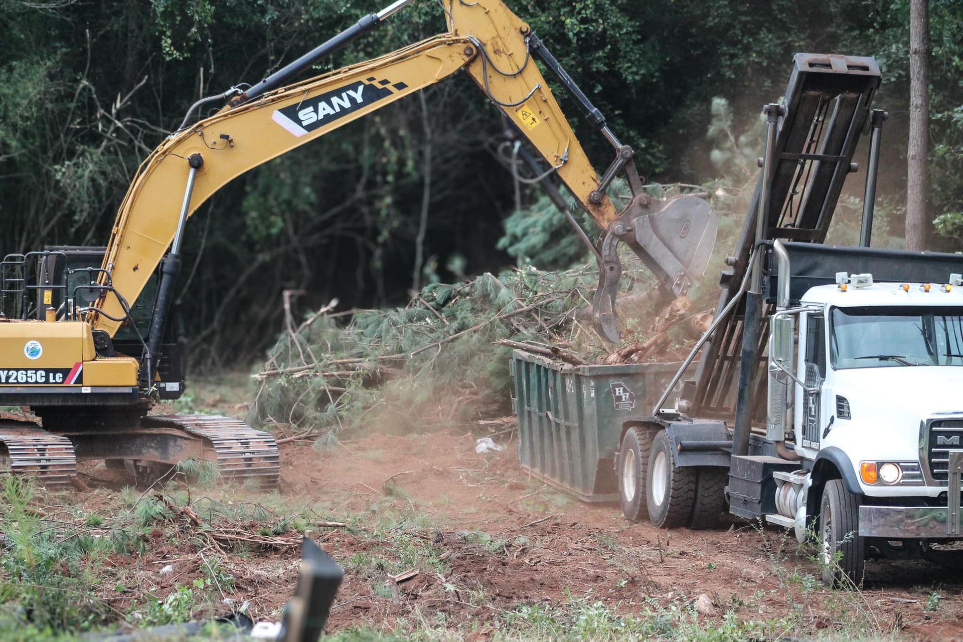 Excavator loading debris into a truck at a wooded construction site
