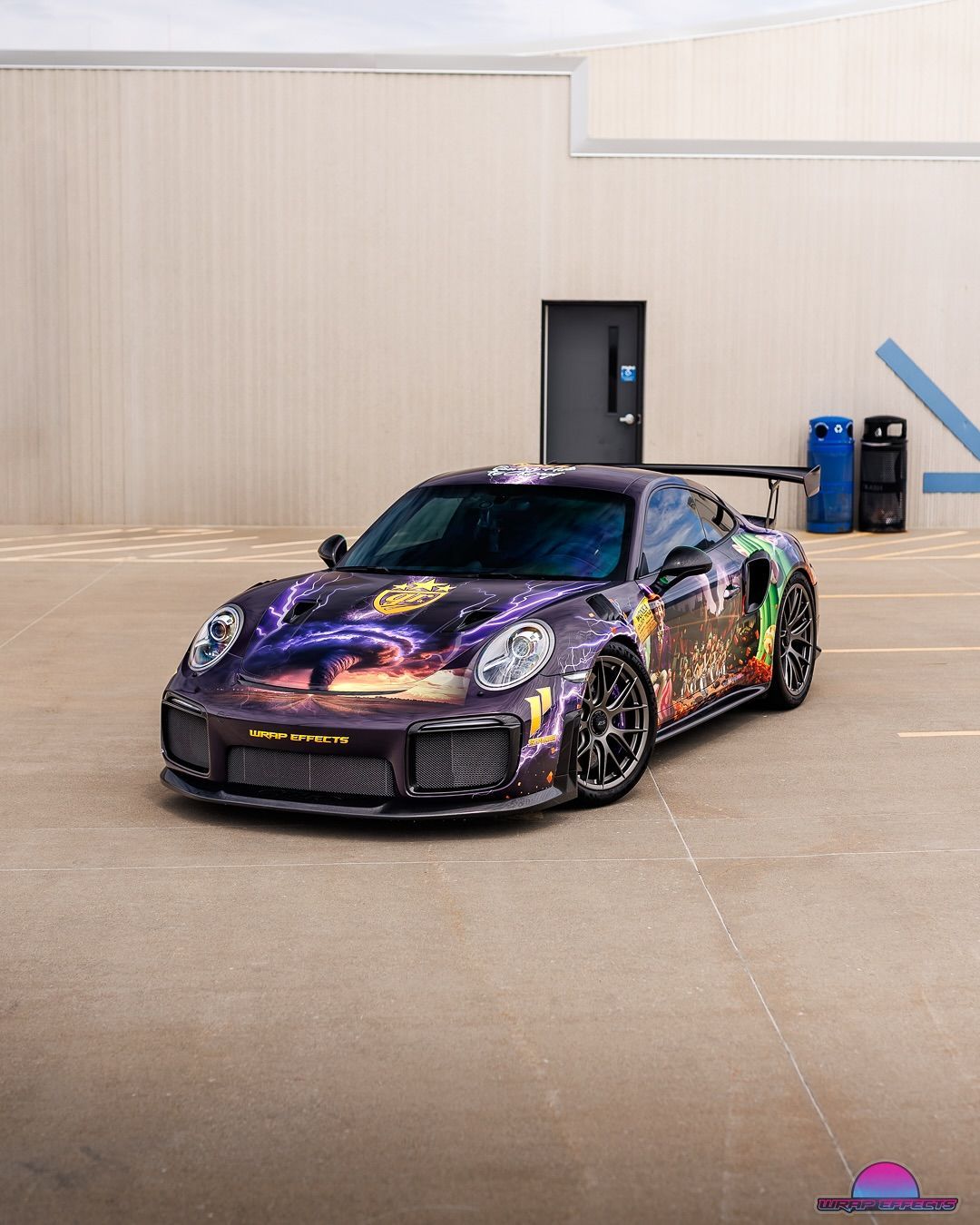 Purple and black Porsche 911 GT2 RS with colorful graphics, parked in front of a white building.