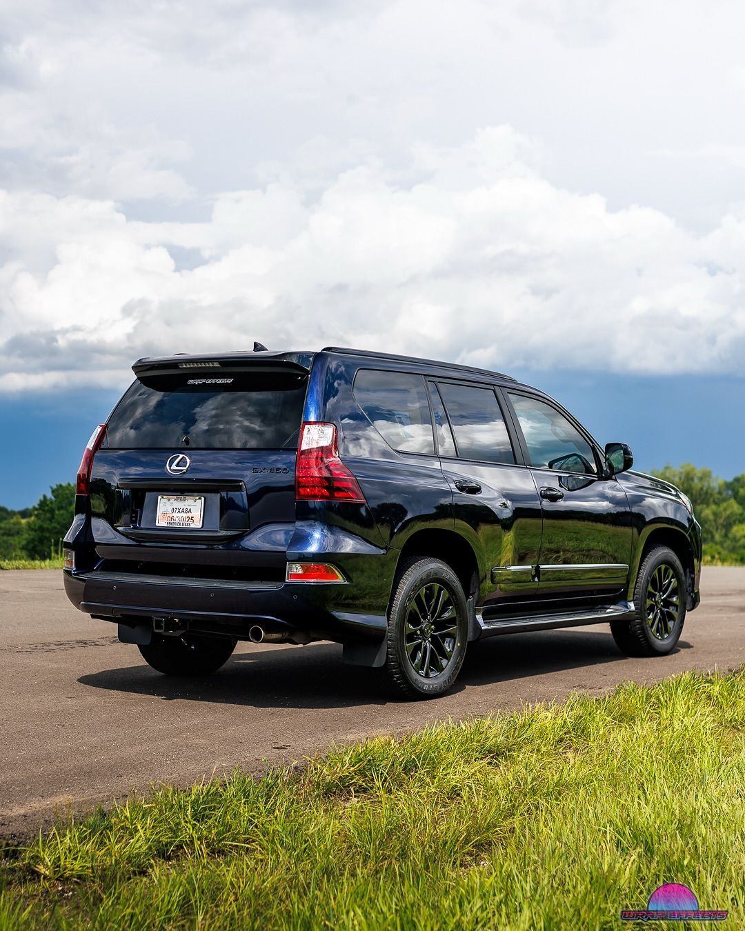 Dark blue Lexus SUV parked on a road with a cloudy sky and green grass.