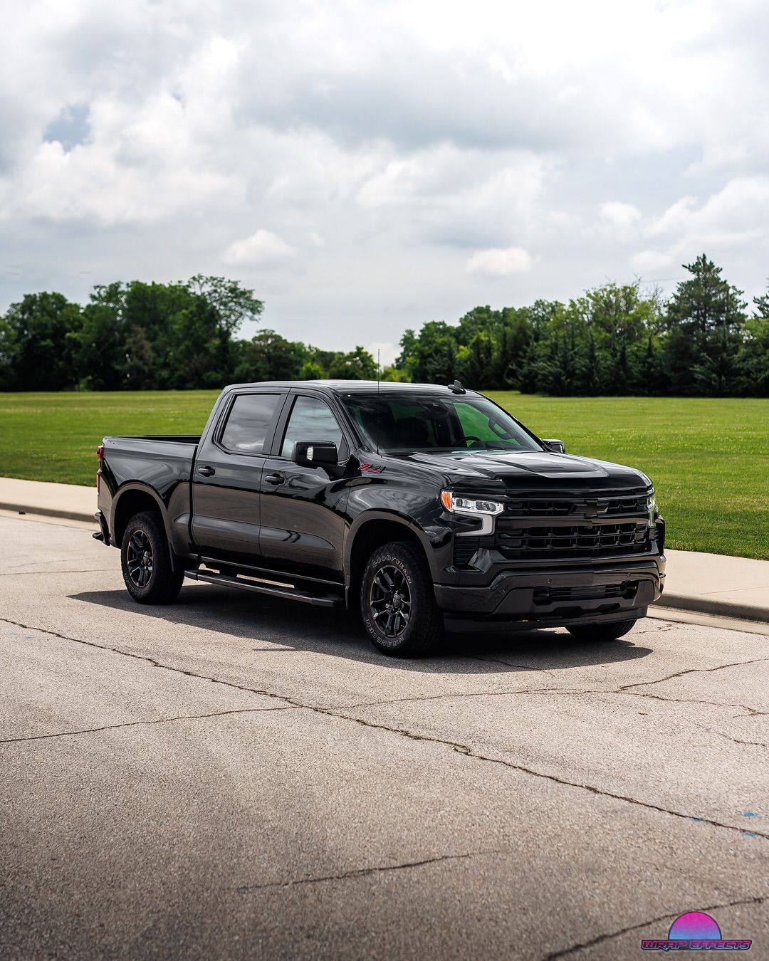 Black Chevrolet pickup truck parked on a paved road with green grass and trees in the background.