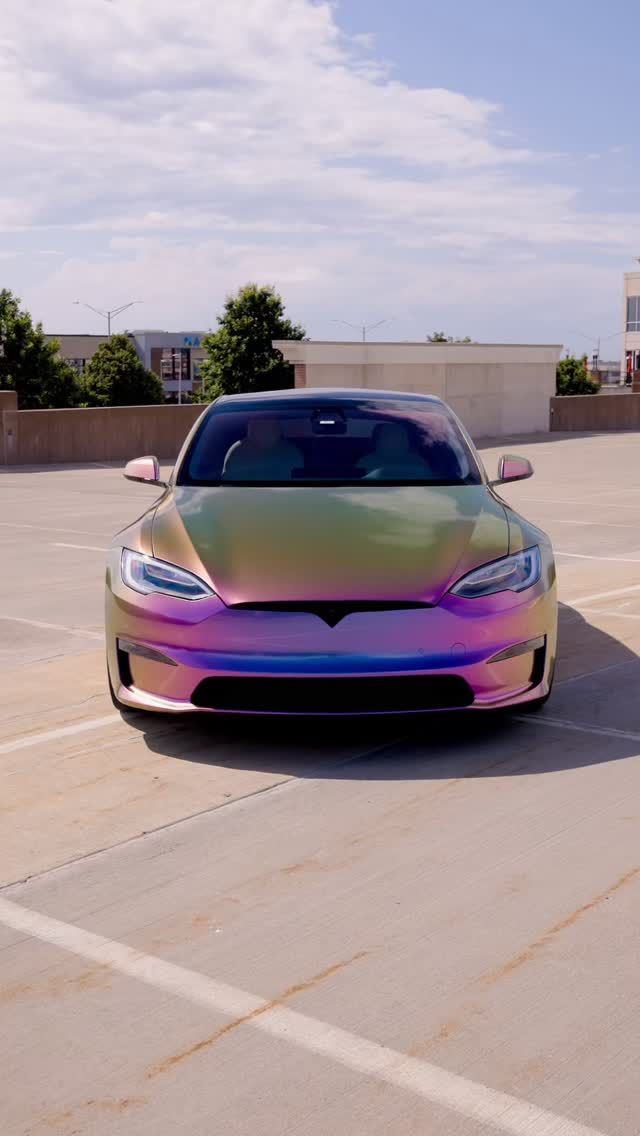 Tesla car with a color-shifting wrap parked on a rooftop parking lot under a blue sky.