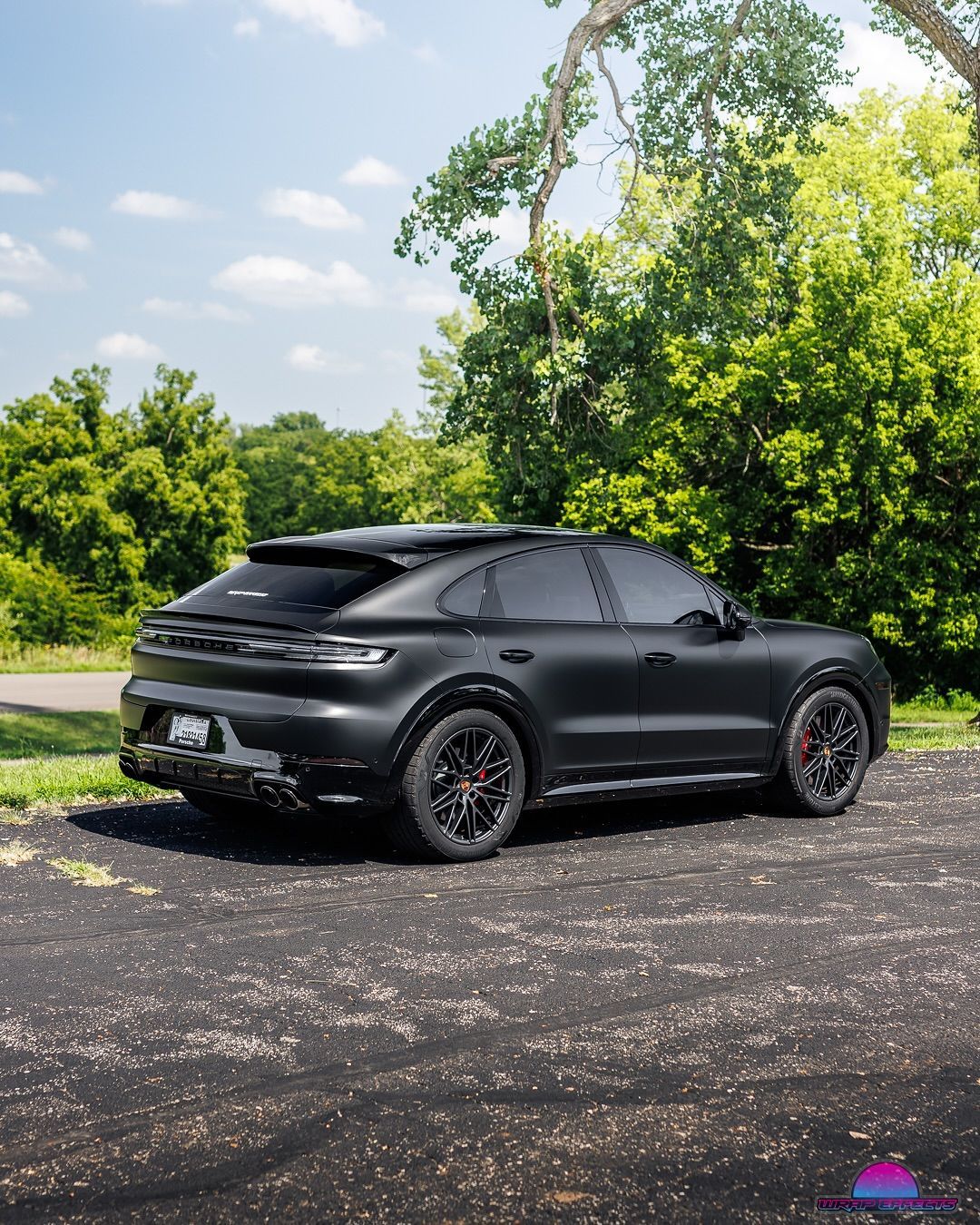 Black Porsche SUV parked on asphalt with greenery in the background.