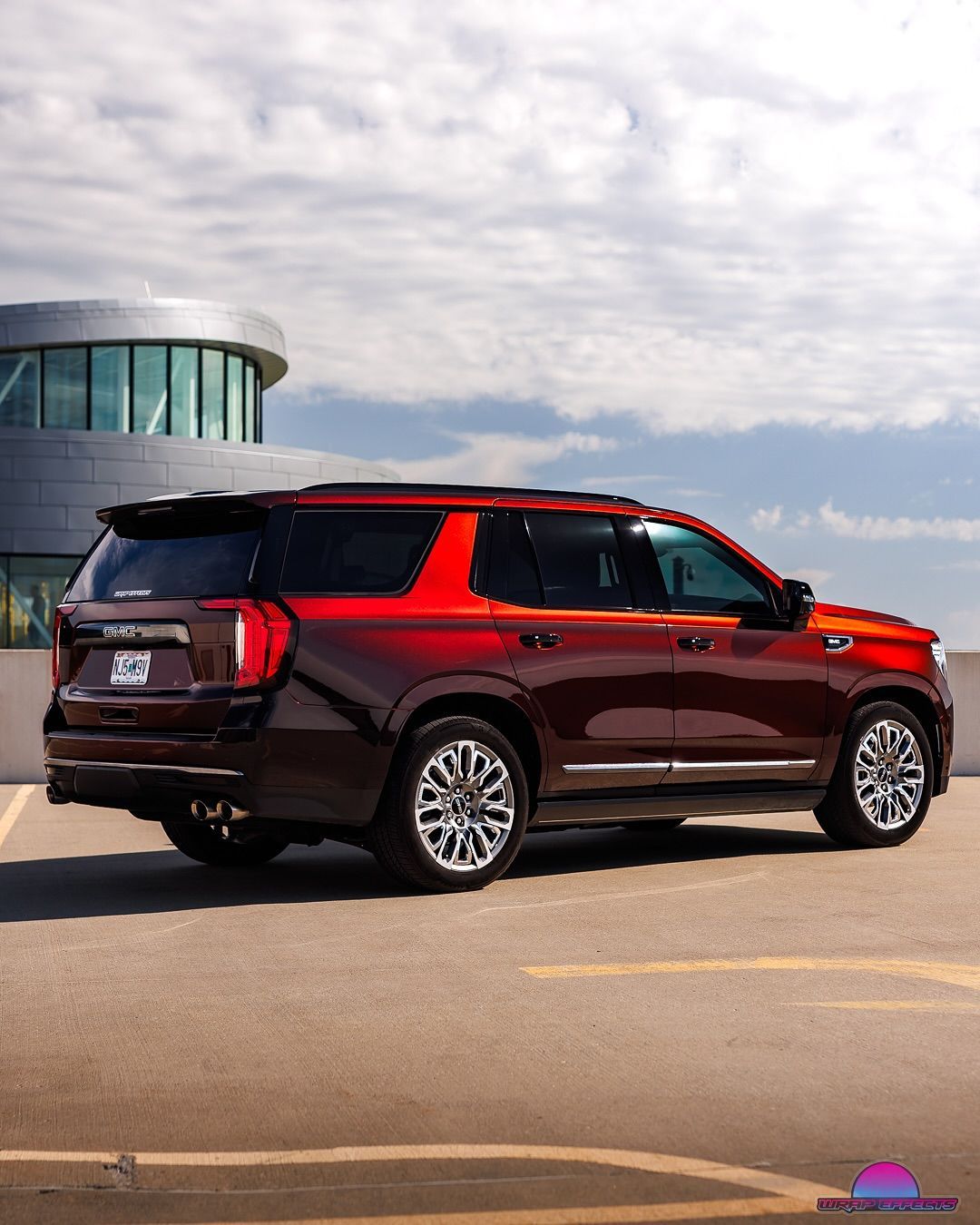 Red GMC Yukon SUV parked in a lot with a modern building in the background under a cloudy sky.