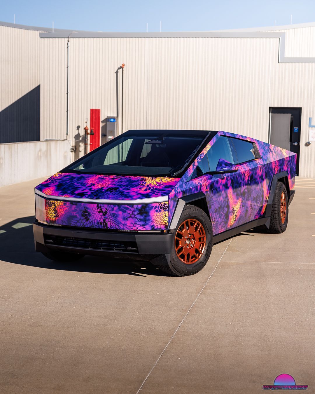 Tesla Cybertruck wrapped in purple galaxy-themed vinyl, parked in front of a building.