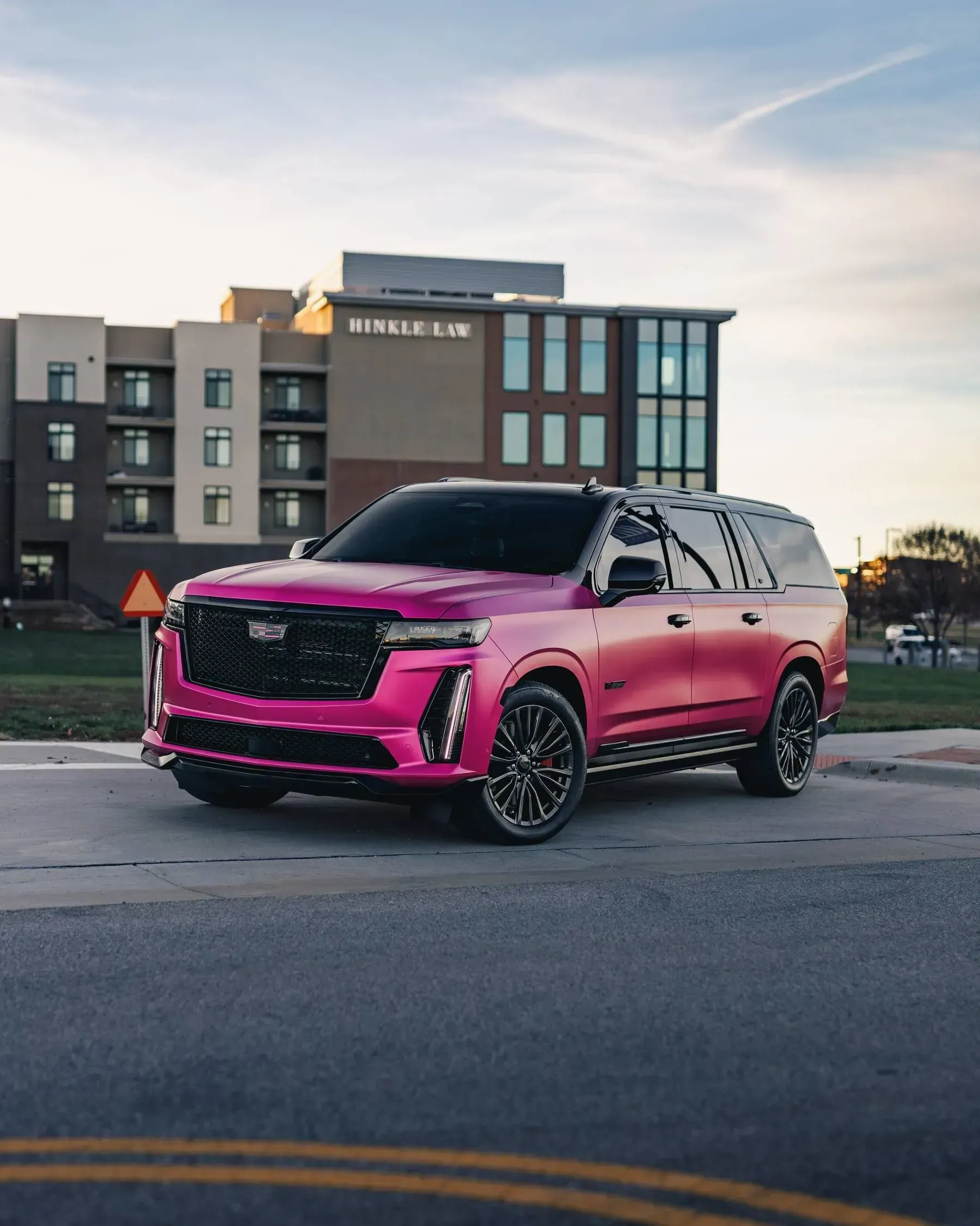 Pink Cadillac Escalade parked in front of a building with dark tinted windows.