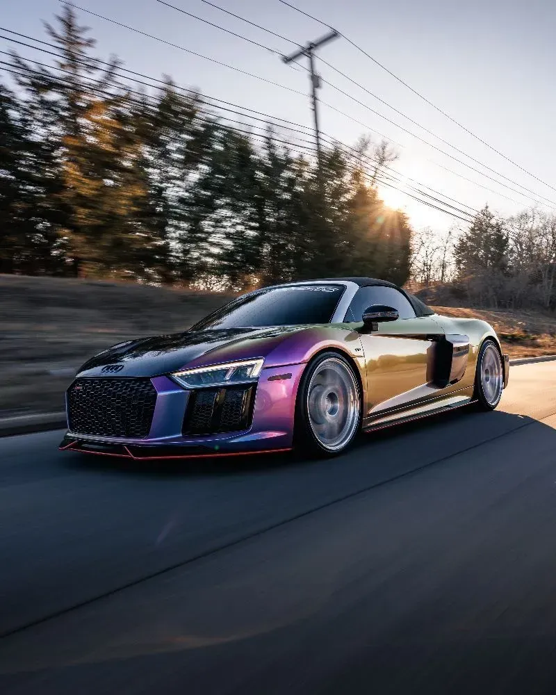 Audi R8 Spyder sports car with iridescent paint, driving on a road with trees.