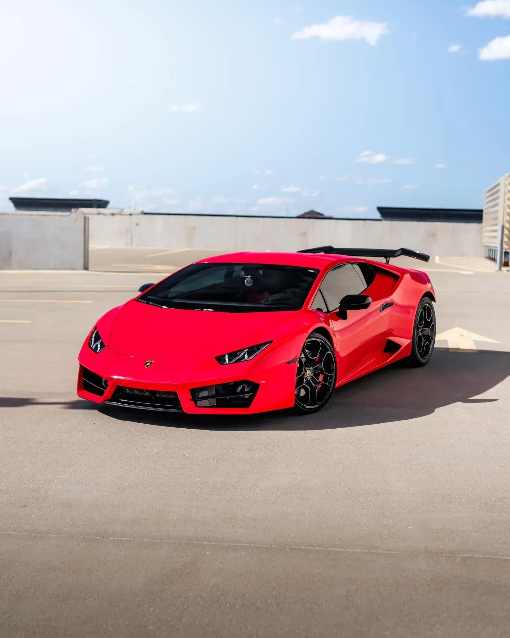 Red Lamborghini sports car parked on a rooftop parking lot with a blue sky in the background.
