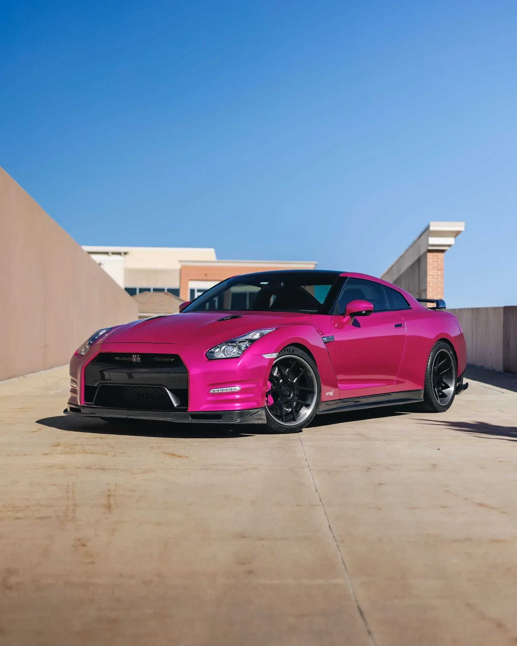 Pink Nissan GT-R sports car parked on a rooftop parking structure with a clear blue sky.