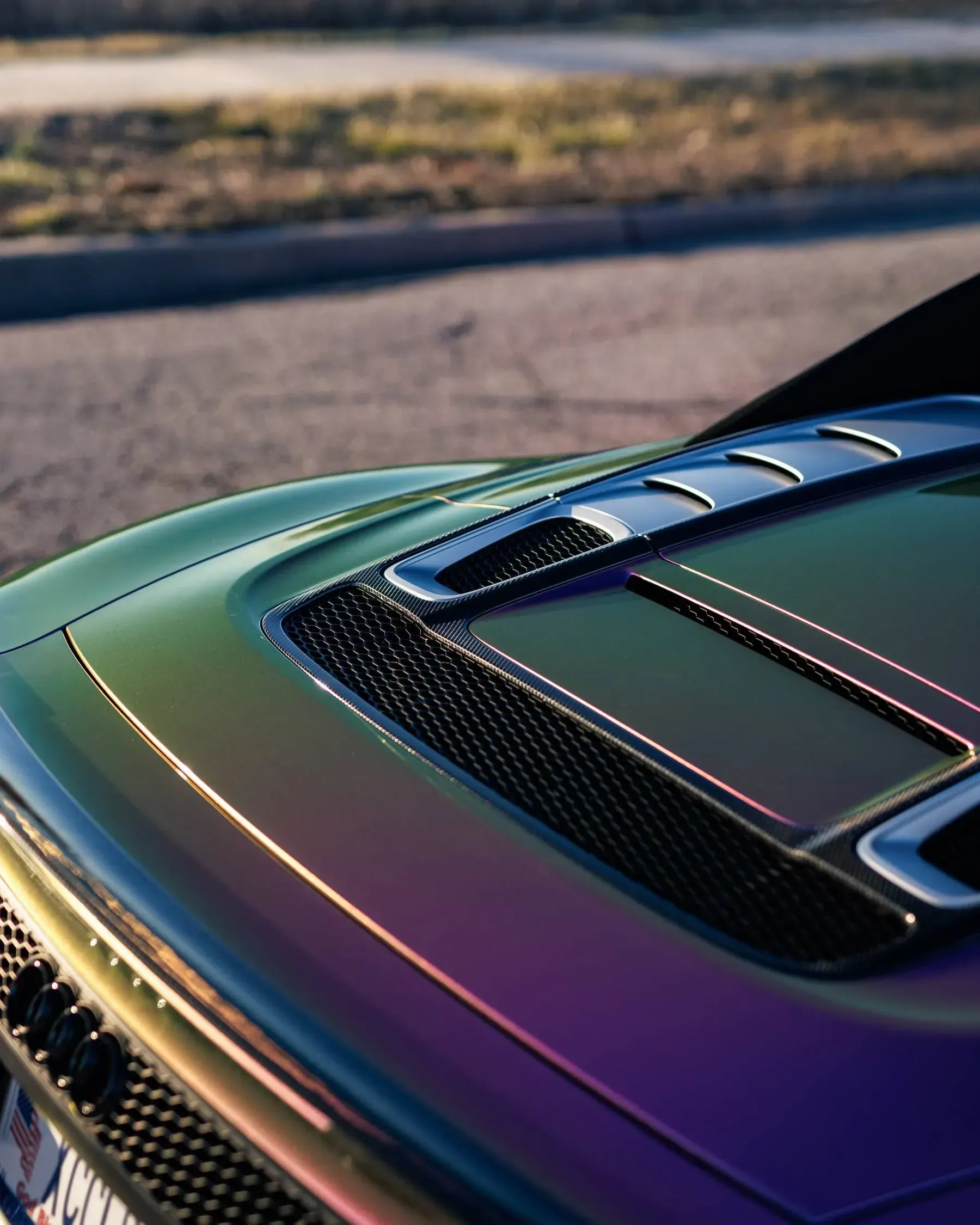 Close-up of a car hood with iridescent paint, featuring air vents and reflective light.