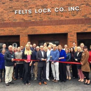 A group of people are standing in front of a felts lock co. inc. building holding a red ribbon.