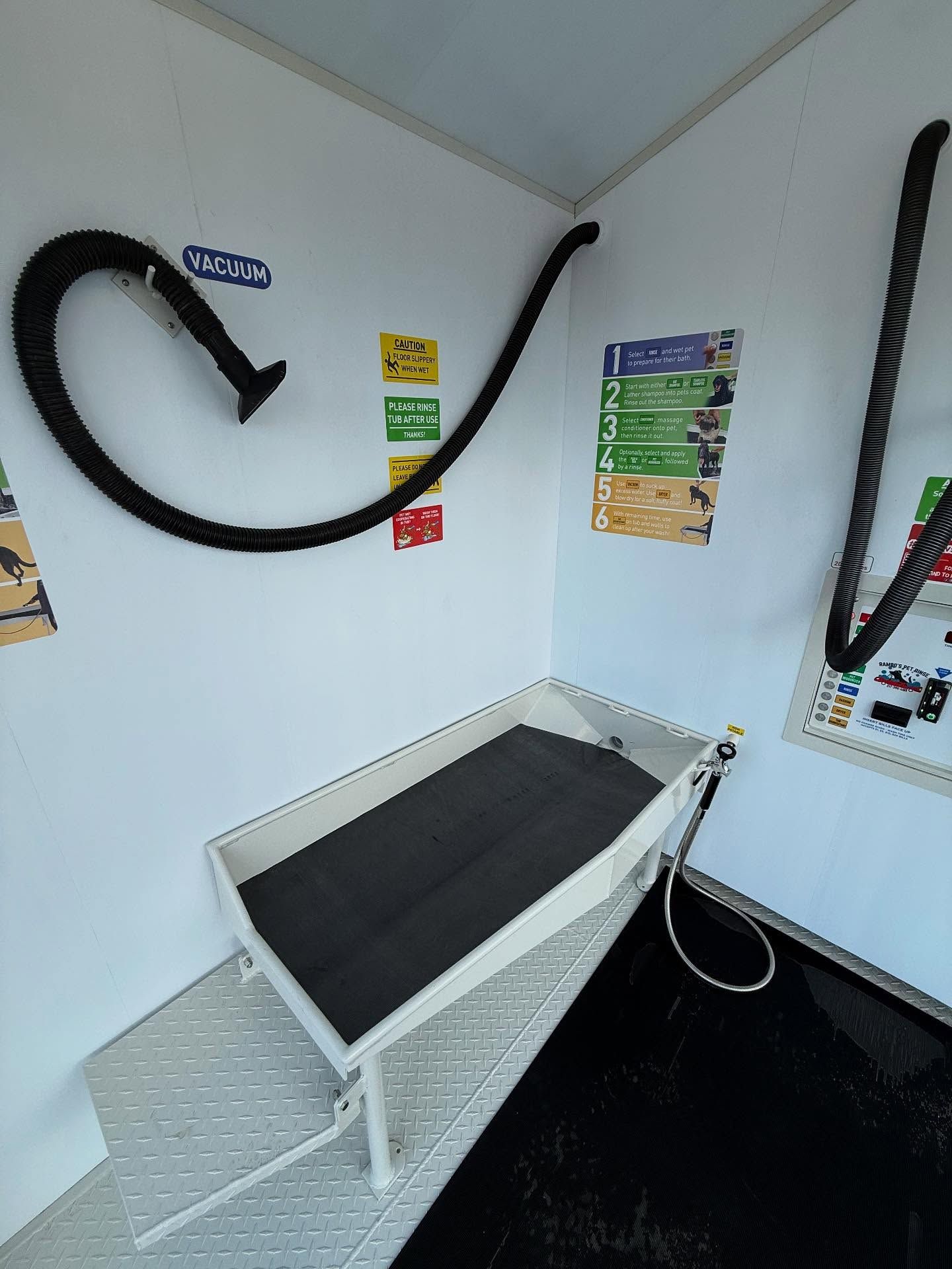 Dog washing station in a trailer. White walls, black mat, flexible hose, and informational posters.