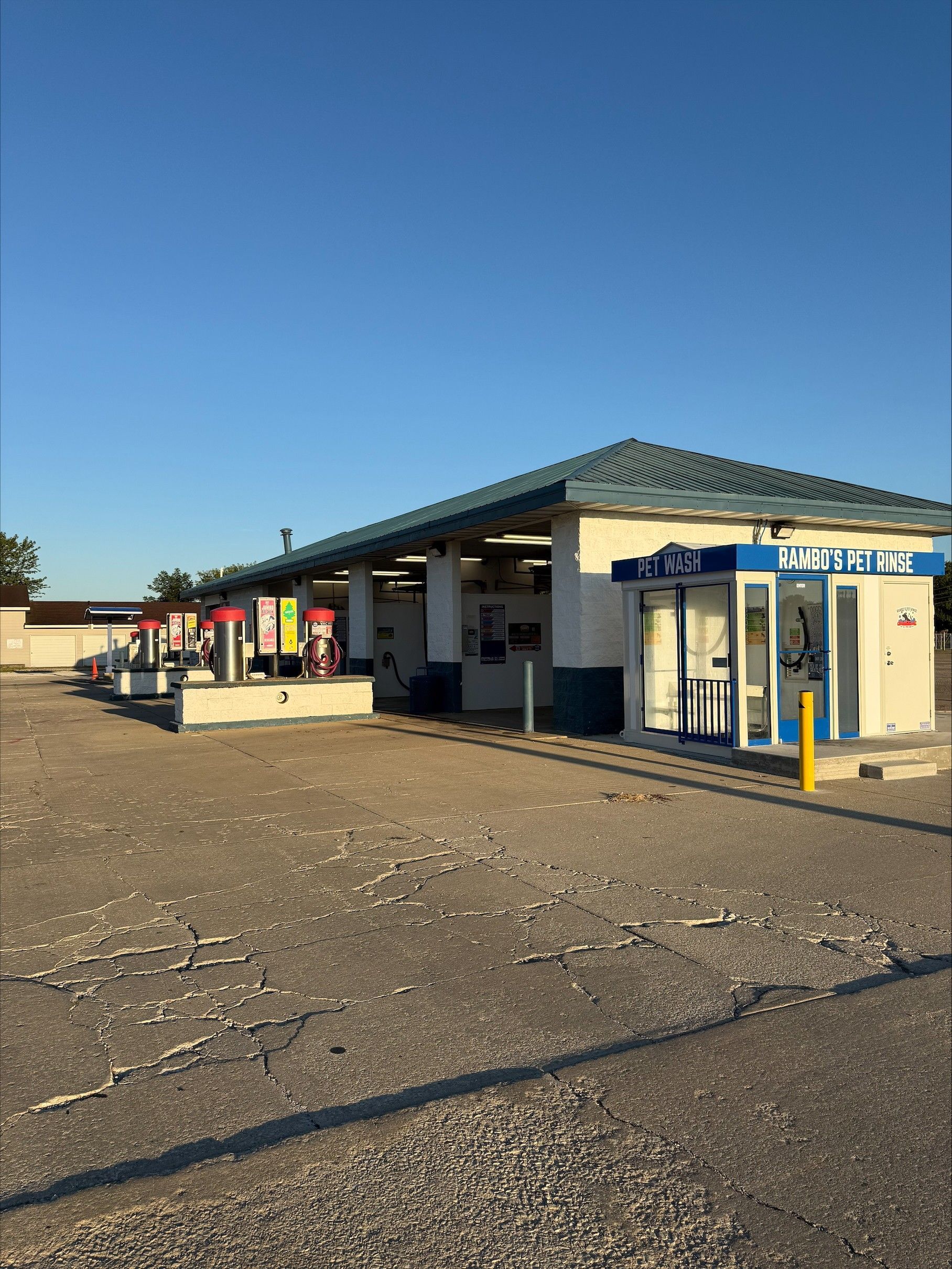 A drive-through car wash with various bays, a blue roof, and a payment kiosk under a clear, blue sky.