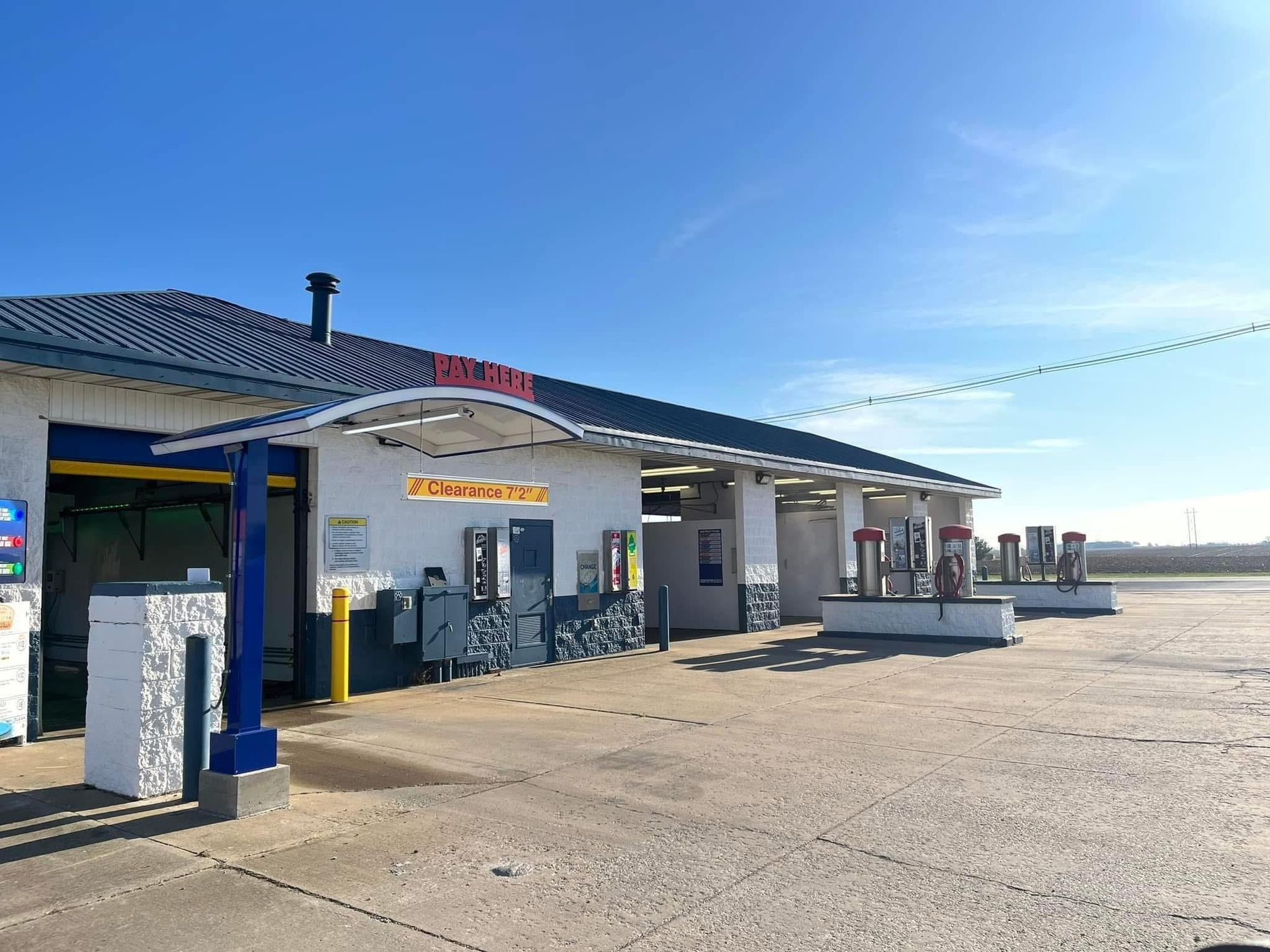 Car wash with blue accents on a sunny day, with multiple wash bays and a sign saying