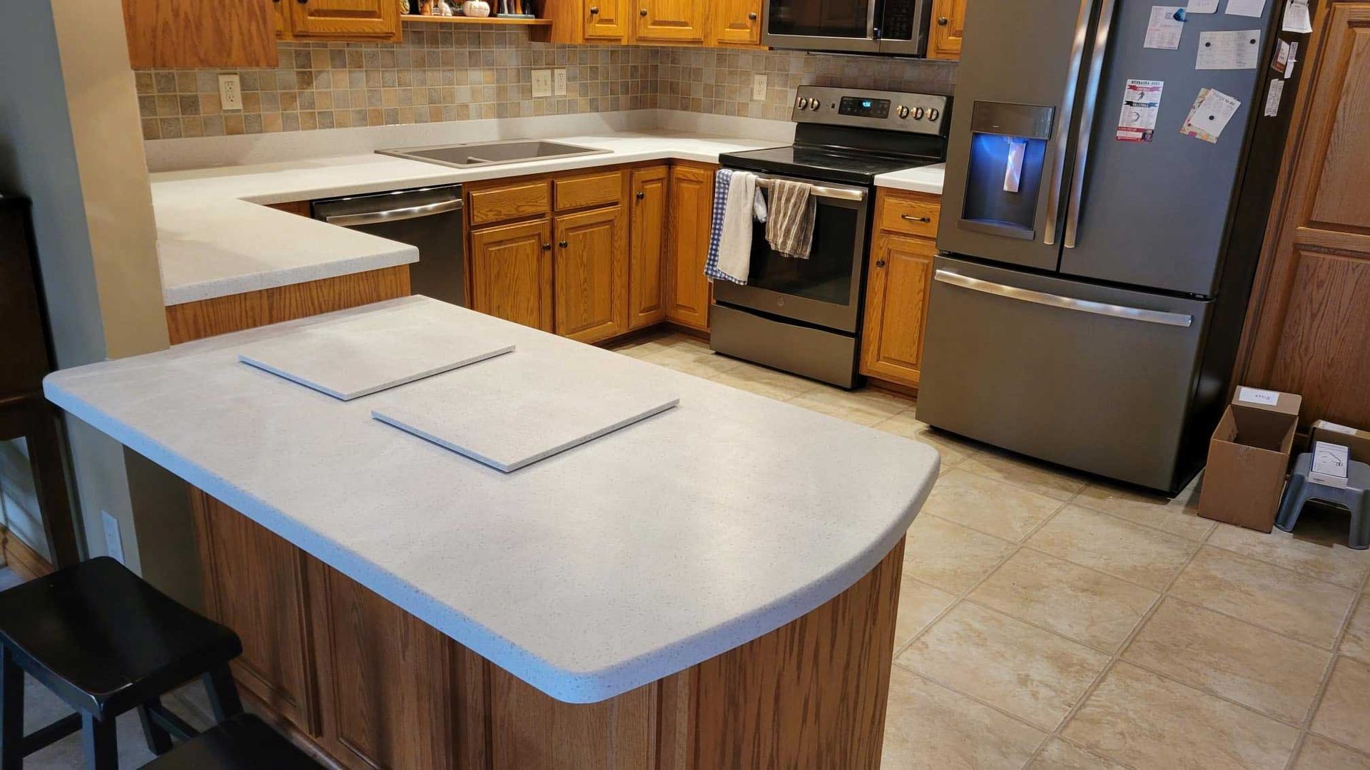 Kitchen with light countertops, wood cabinets, stainless steel appliances, and a breakfast bar.