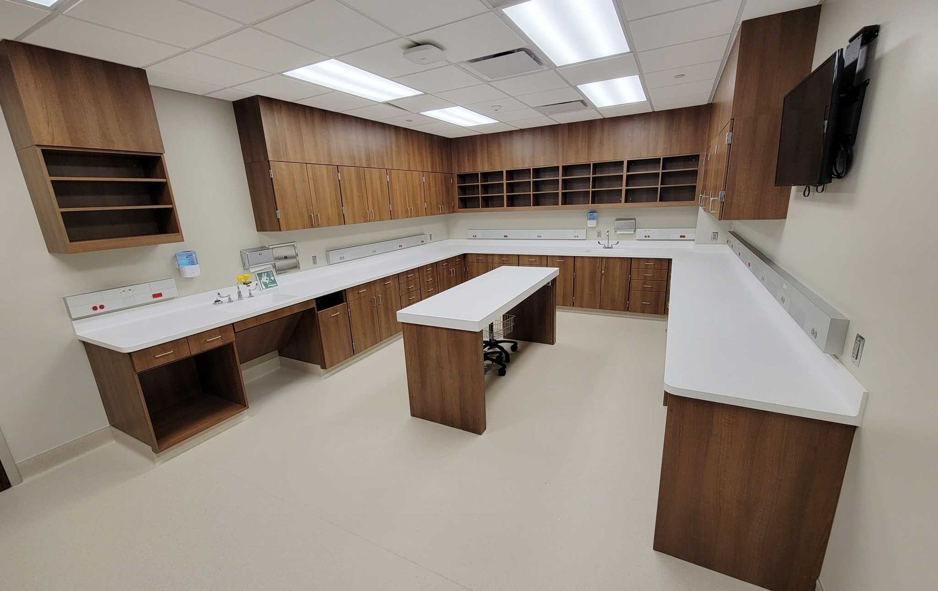 U-shaped workspace with brown cabinets, white countertops, and open shelves; a television is on the wall.