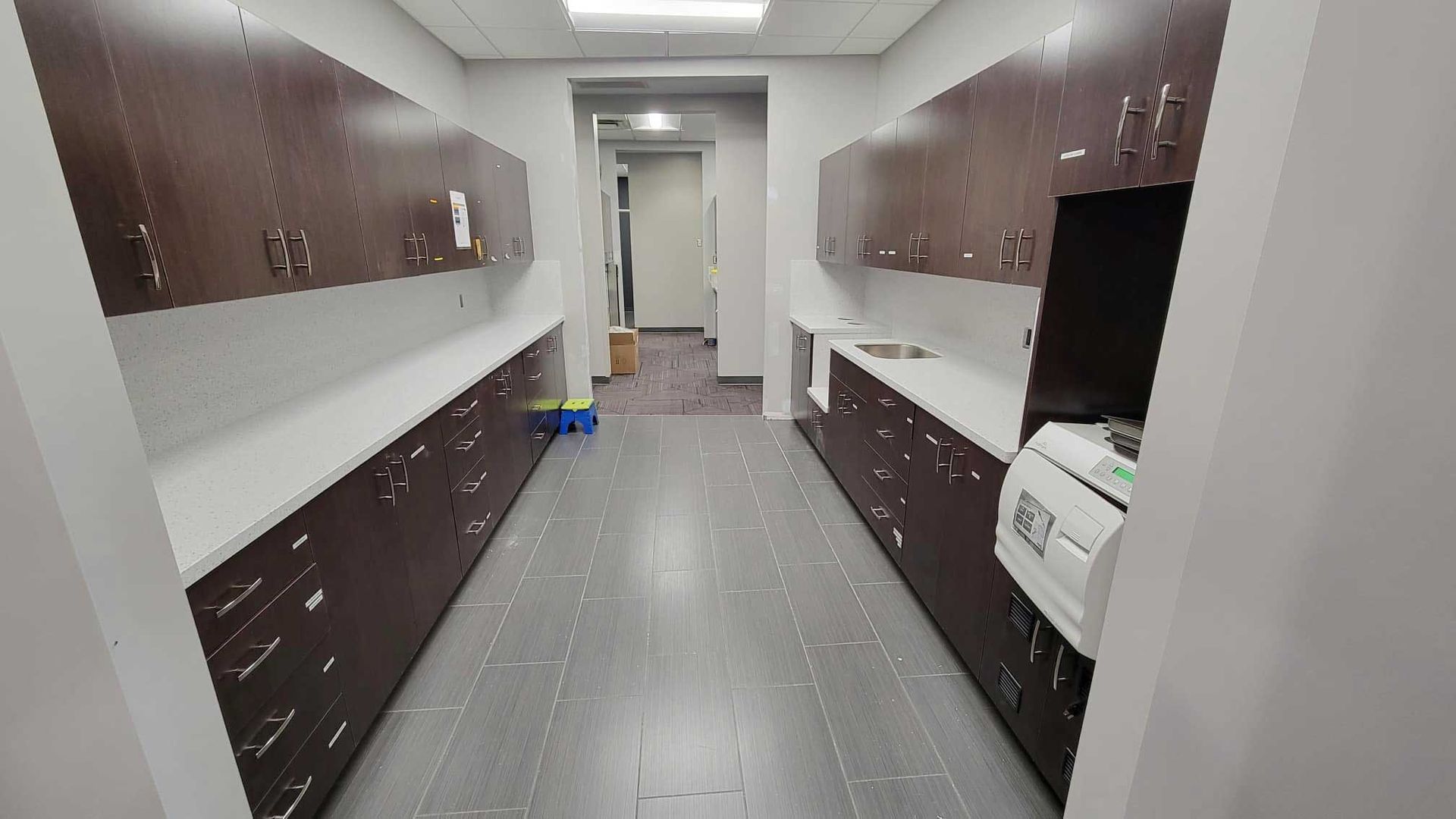 Long, narrow room with dark brown cabinets, light countertops, and gray flooring.