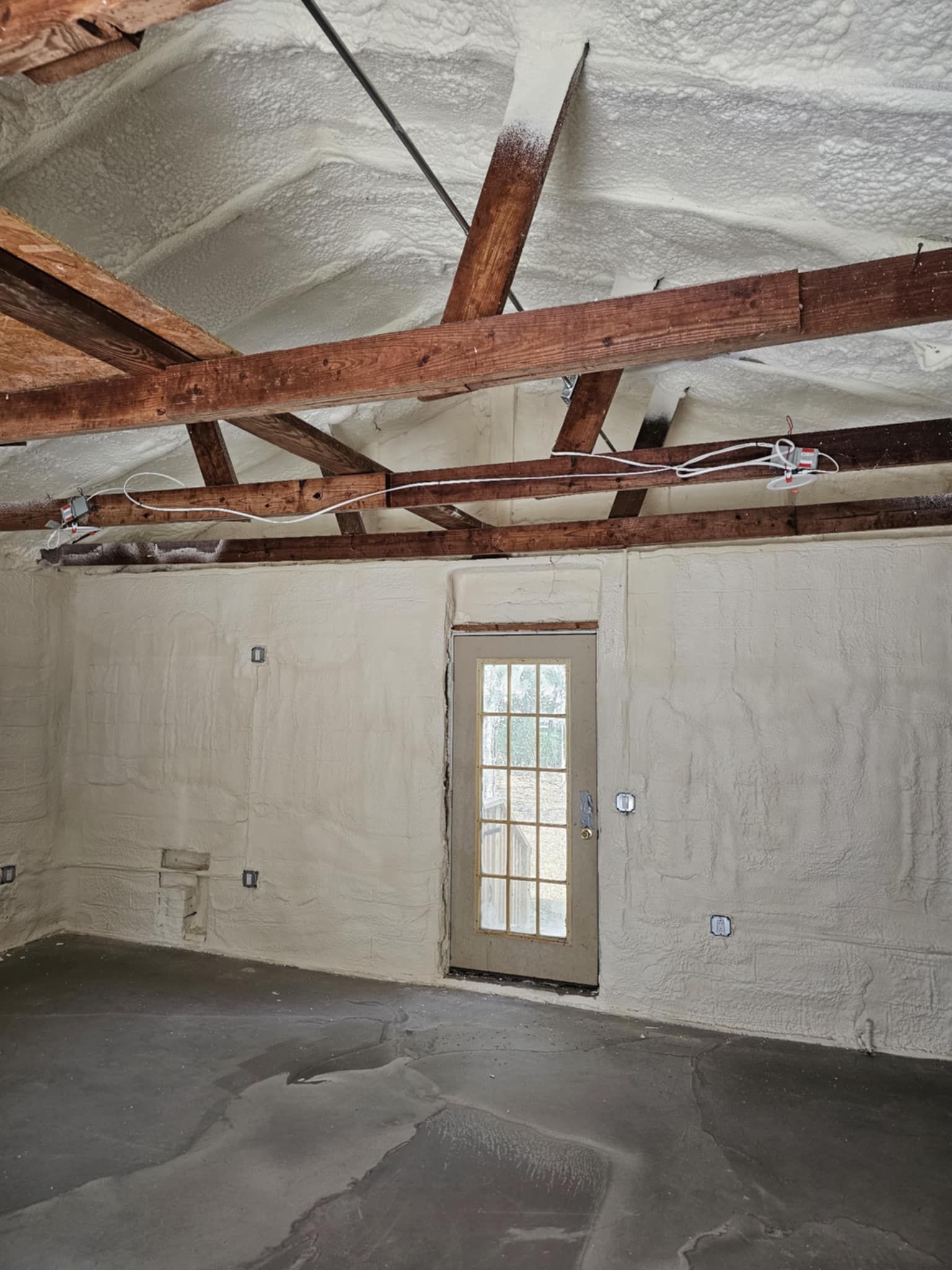 An empty room with a door and wooden beams covered in spray foam.