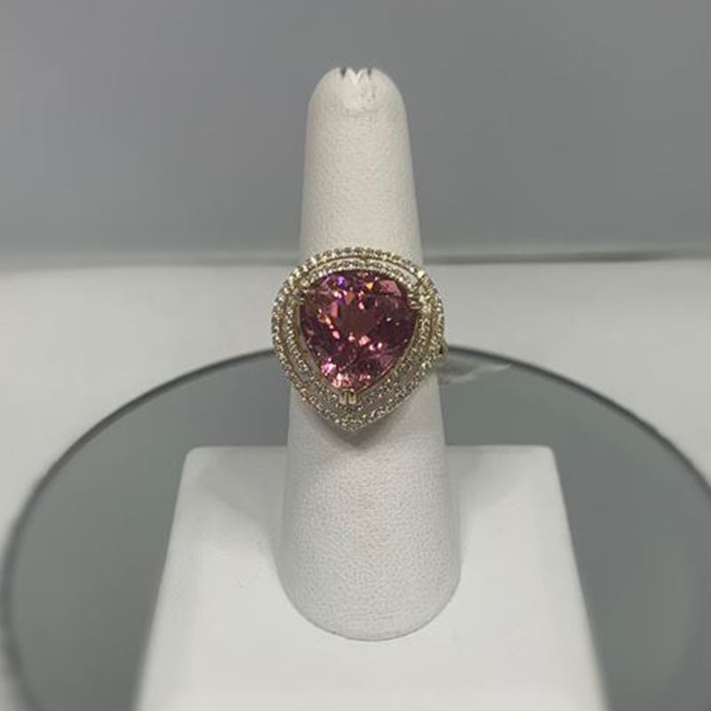 A pink heart shaped ring is sitting on a white ring holder.