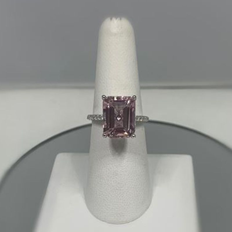 A pink diamond ring is sitting on a white ring holder.