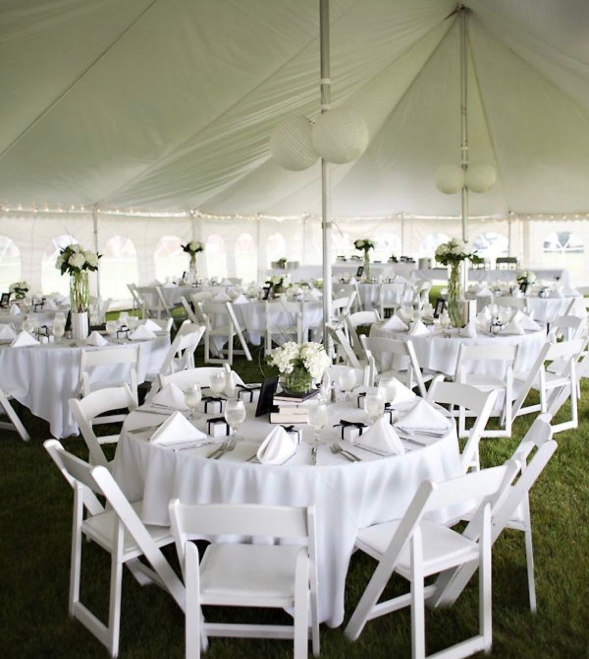 Round tables and chairs arranged inside a large white event tent with floral centerpieces