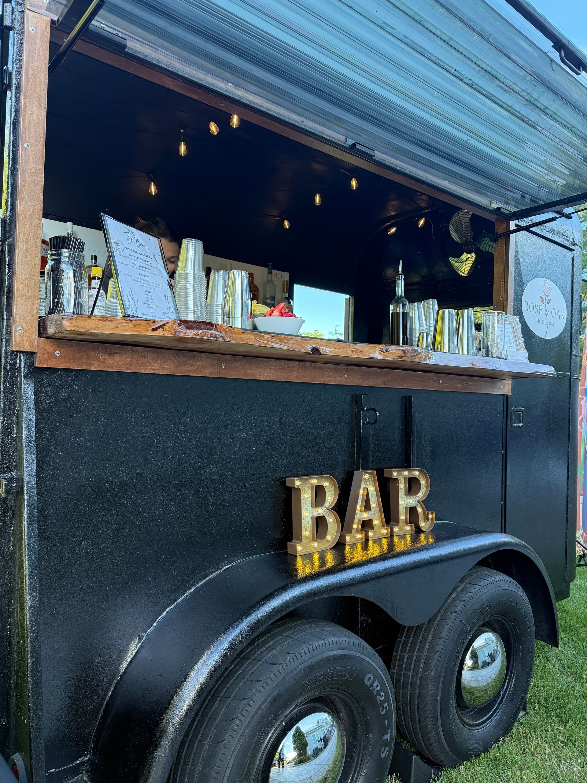 Compact black mobile bar trailer with open service window, and wooden counter.