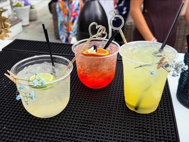 Three colorful signature cocktails on a bar tray, garnished with flowers and citrus slices.