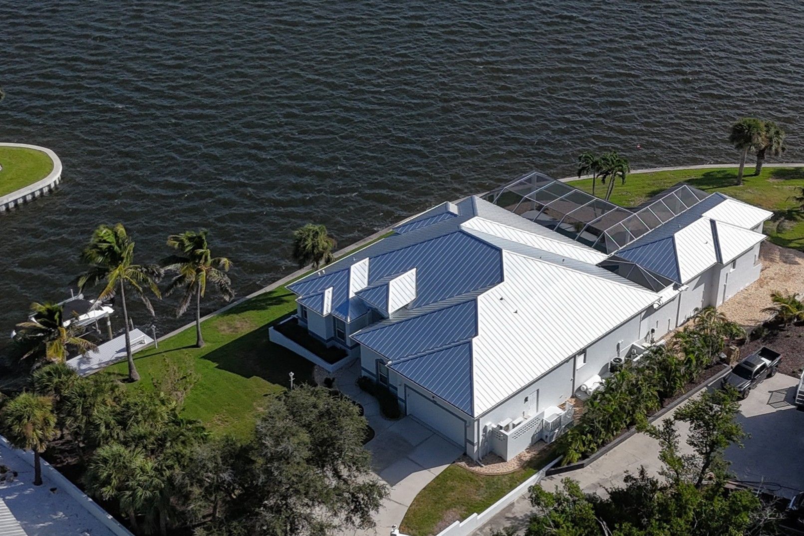 Aerial view of a white waterfront house with solar panels on the roof, next to the water.