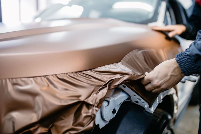 Person wrapping a car bumper with brown protective film.