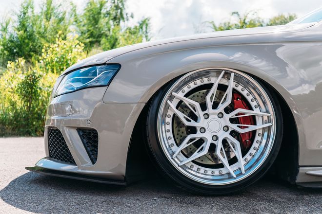 Low-slung gray sports car with chrome rims parked outdoors.
