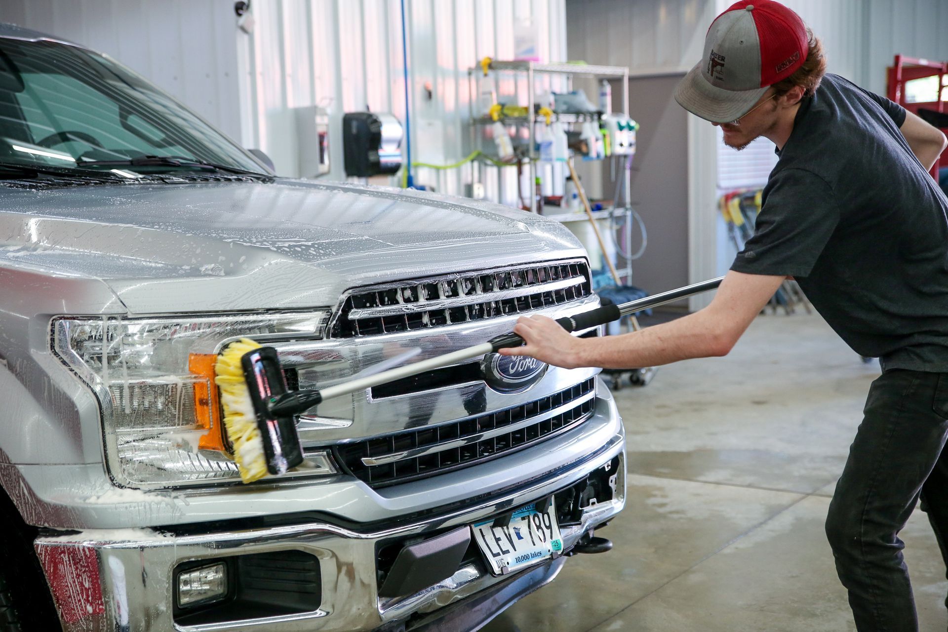 Person washing a silver Ford truck, using a brush on a long handle.