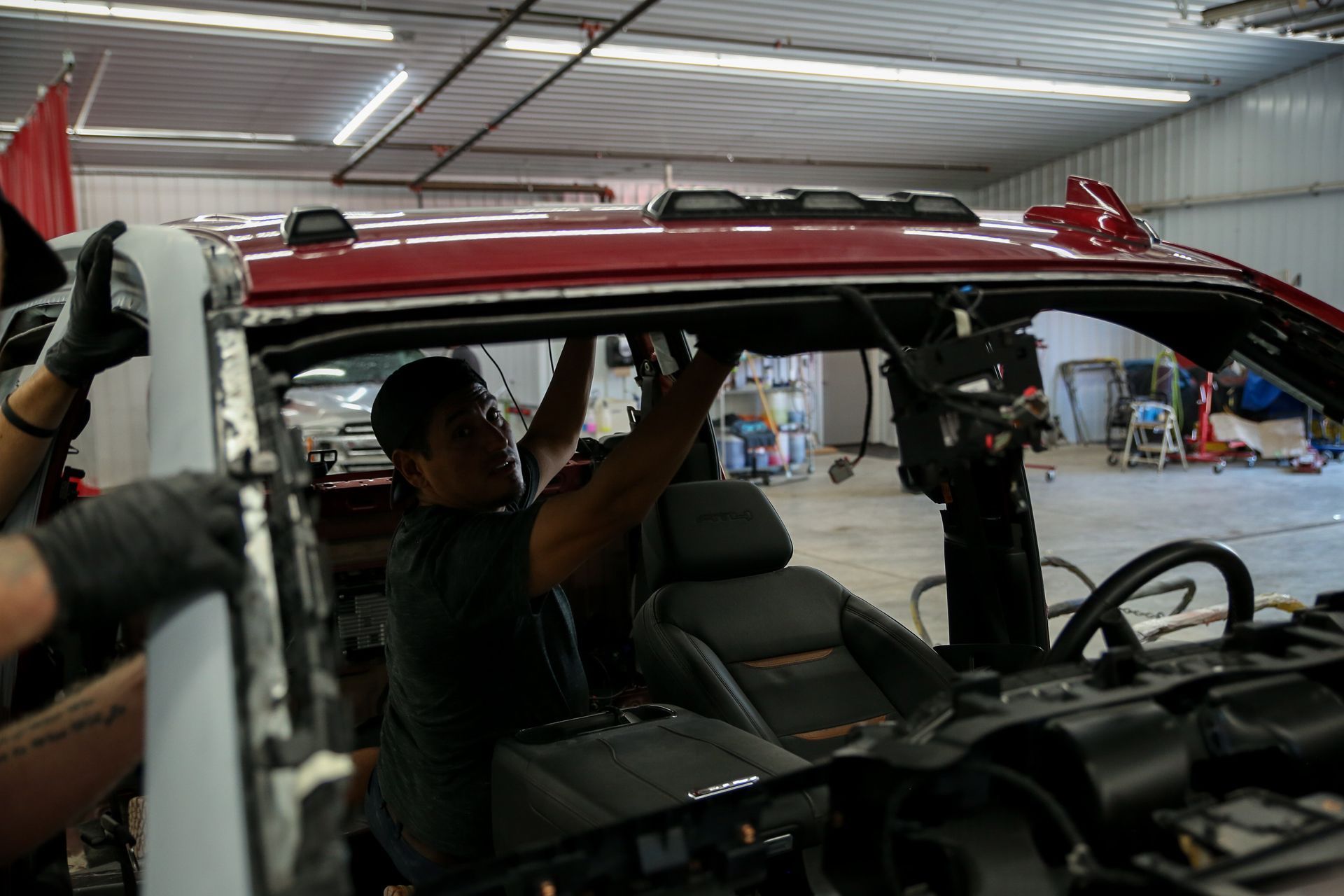 People installing a red truck roof in a garage, with the interior visible. Two workers are reaching toward the roof.