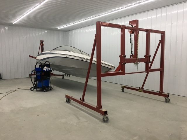 A boat suspended in a workshop by a red lift. A welder is nearby.