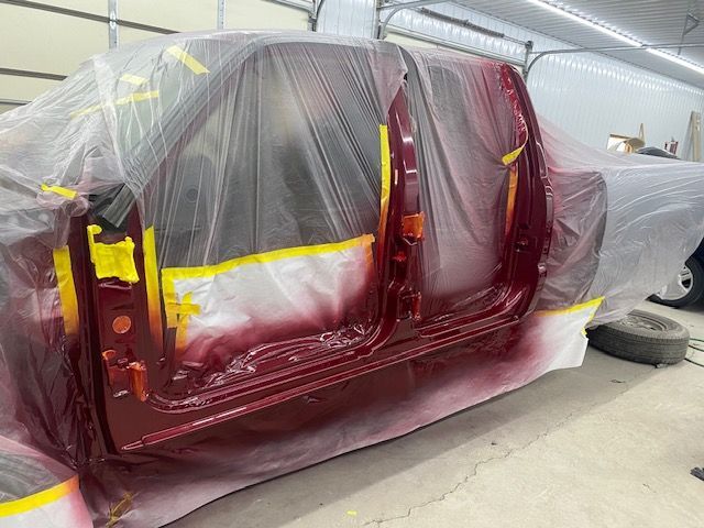 Red truck doors being painted inside a shop, covered with plastic sheeting and yellow tape.