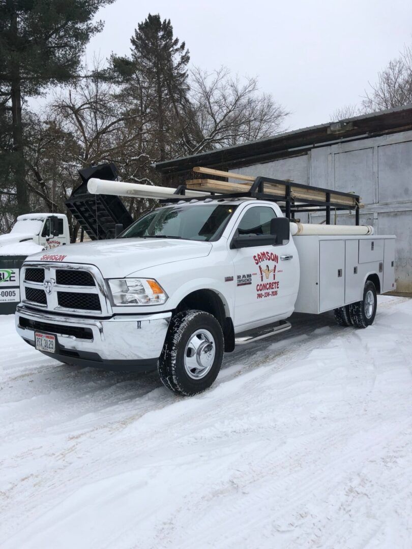 A white truck is parked in the snow in front of a building.