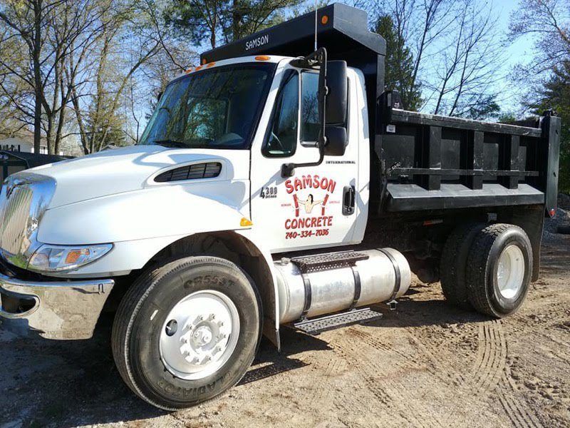 A white dump truck from sanson concrete is parked in a dirt lot.