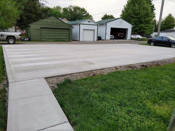 A concrete driveway with a sidewalk and a garage in the background.