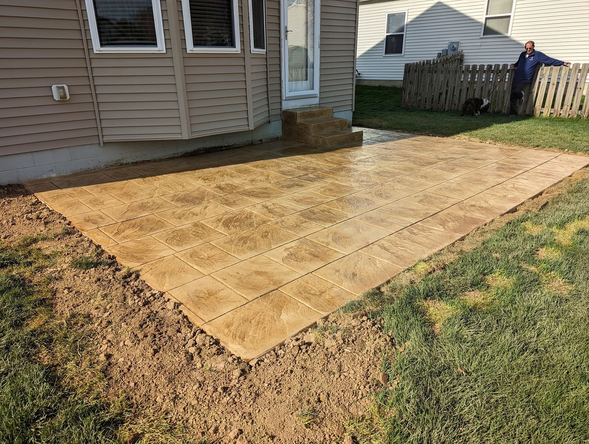 A man is standing next to a concrete patio in front of a house.